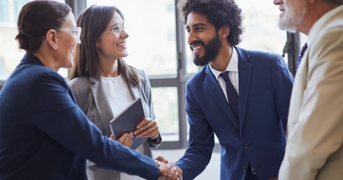Group of professionally dressed colleagues smiling and shaking hands in a bright office environment.